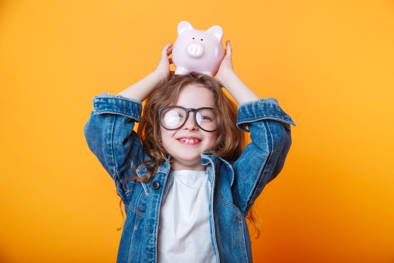 Cute little girl in eyeglasses shaking piggy box