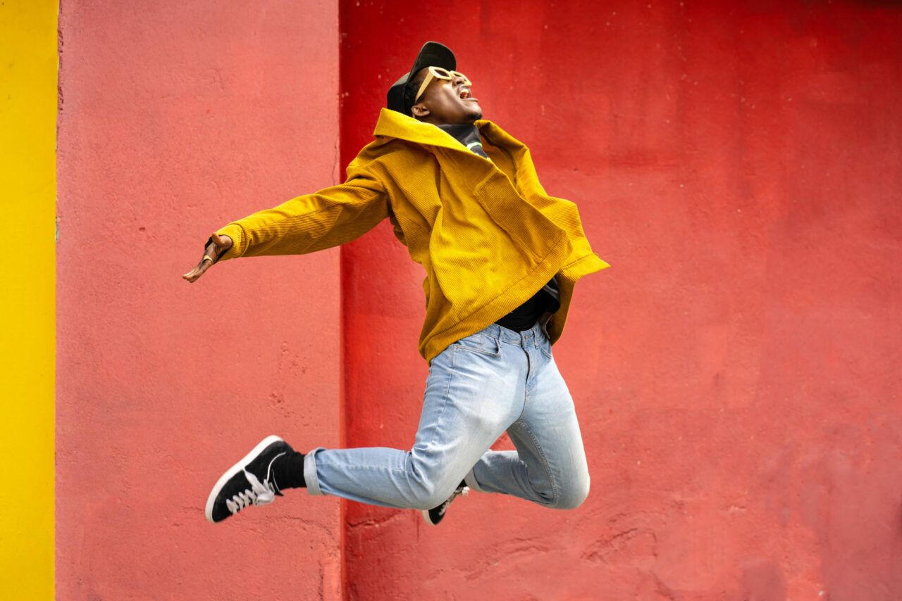 A girl in athletic wear jumping in the air at the top of a mountain range, down below is a stream of water in between mountains.