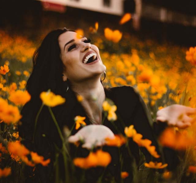 Young girl smiling with her hands up beside her looking up at the sky sitting in a feild of orange flowers